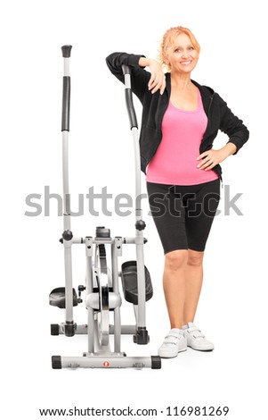 Full length portrait of a mature female posing next to a cross trainer isolated on white background