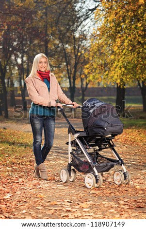A young mother pushing a baby stroller in a park in autumn