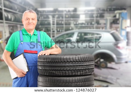 Mature auto mechanic posing on a tires in front of car during automobile maintenance at auto repair shop