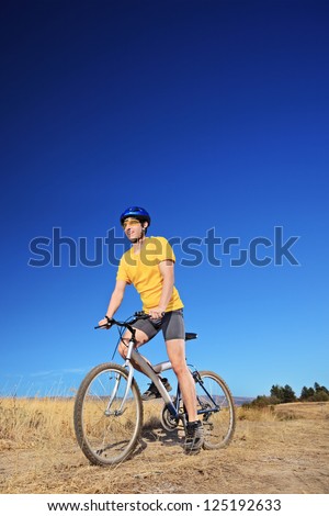 Panning shot of a bicycle rider riding a bike outdoors on a sunny day against a blue sky