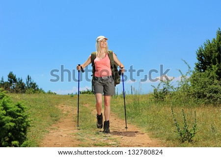 A young woman with backpack and hiking poles walking in the mountain