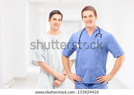 A male medical practitioner in a uniform and a patient in hospital gown posing in a clinical corridor