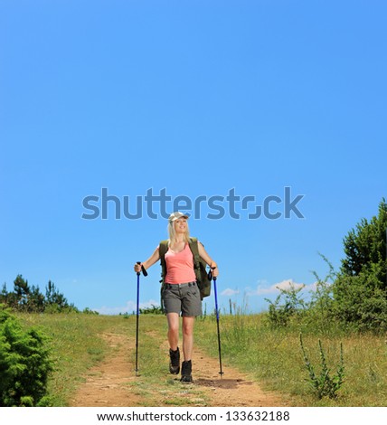 A young female with backpack and hiking poles walking in the mountain