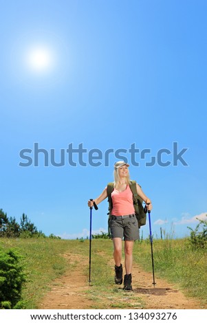 Young woman with backpack and hiking poles walking at sunny day in the mountain