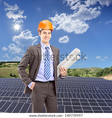 Architect wearing helmet and holding blueprints, with solar photovoltaic cell panels in the background, shot with a tilt and shift lens