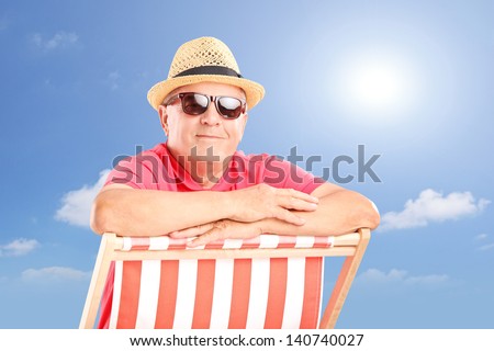 Smiling mature man wearing hat and sunglasses, posing on a beach chair on a sunny day
