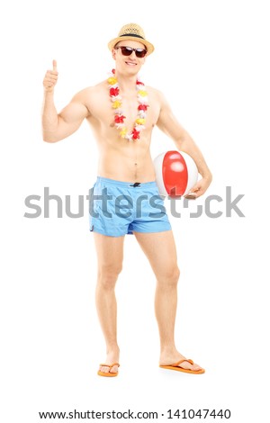 Full length portrait of a male in swimming shorts, holding a beach ball and giving thumb up, isolated on white background