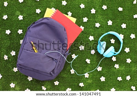 School backpack with books and headphones on a green grass with daisy flowers