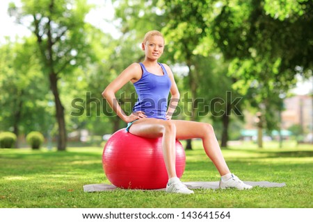 Young female athlete sitting on a  pilates ball and looking at camera in park