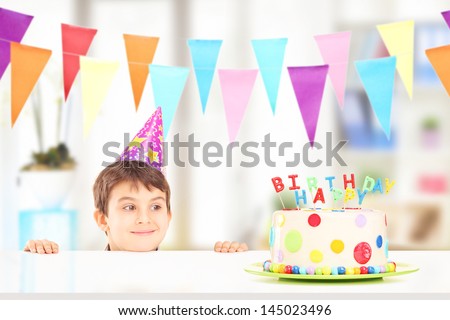 Smiling boy with party hat looking at a birthday cake at home