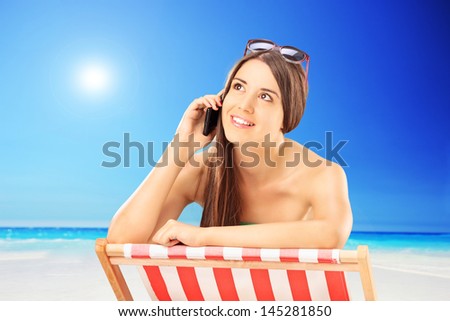 Beautiful female on a chair talking on a mobile phone, outside on a sunny day
