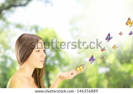 Beautiful young female with many colorful butterflies on her hand, posing outside in a park