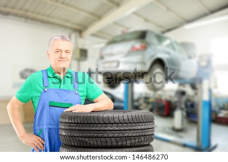 Auto mechanic posing on tires in front of car during automobile maintenance at auto repair shop
