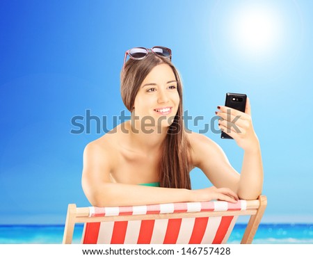 Beautiful female on a beach chair looking at mobile phone, outside on a sunny day