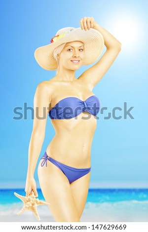Smiling female in bikini holding a starfish and posing on a beach enjoying the sun