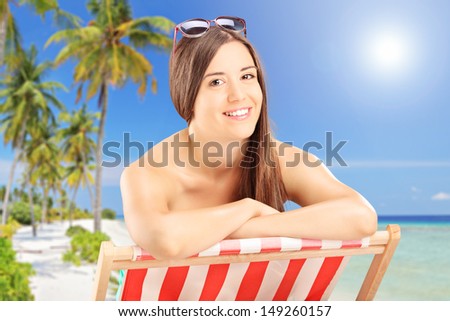 Young smiling female posing on a beach chair and enjoying the sun, next to a sea