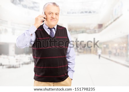 Smiling gentleman talking on a mobile phone and posing in a shopping center