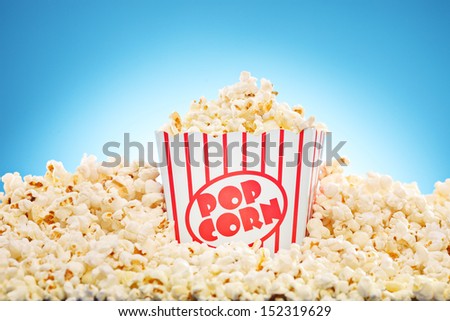 Popcorn in classic box overflowing with freshly popped corn against a blue background