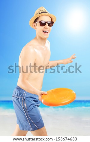 Smiling guy in swimming shorts throwing frizbee, on a beach enjoying the sun