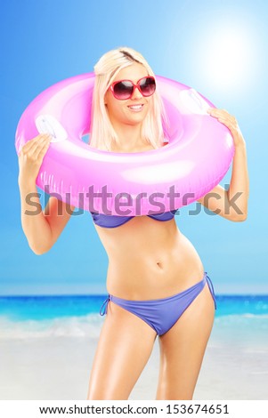 Blond sexy female in bikini holding a pink swimming ring and enjoying on a sunny day on a beach