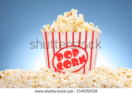 Popcorn in box overflowing with freshly popped corn against a blue background