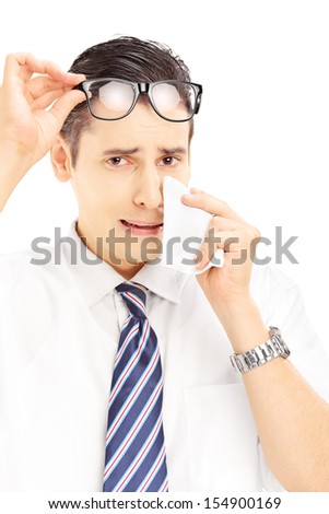 Sad young male wiping his eye from crying with tissue and looking at camera isolated on white background