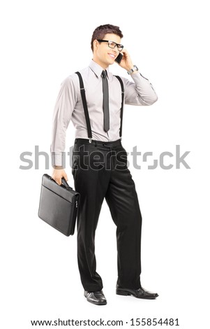 Full length portrait of a young stylish man holding a briefcase and talking on a mobile phone isolated on white background
