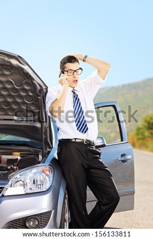 Young nervous male on a broken car talking on a mobile phone
