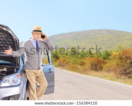 Nervous senior man on a broken car talking on a cell phone, shot with a tilt and shift lens