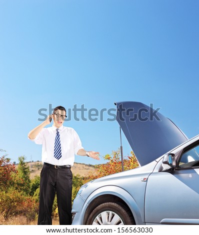 Young businessman standing near a broken car and talking on a mobile phone, shot with a tilt and shift lens