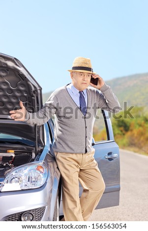 Nervous senior man on a broken car talking on a mobile phone