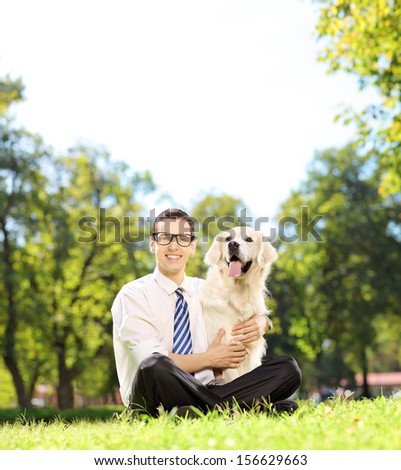 Man sitting on a green grass and hugging his labrador retriever dog in a park, shot with a tilt and shift lens