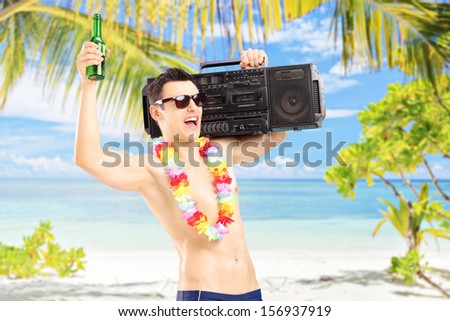 Happy guy with beer and boombox on his shoulder gesturing happiness on a tropical beach