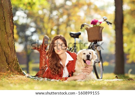 Pretty young female lying down with labrador retriever dog in a park
