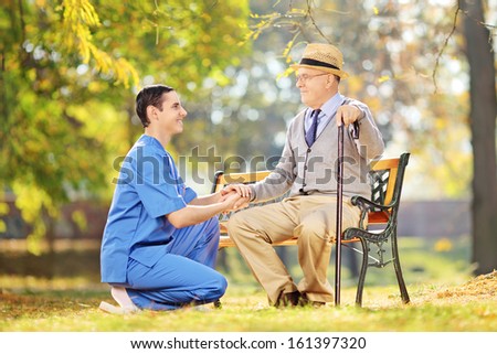 Healthcare professional helping senior man sitting on a wooden bench outside