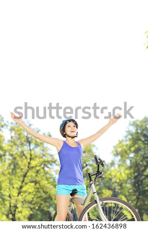 Happy female biker posing with raised hands on a mountain bike in a park