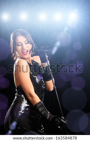 Young woman in black dress on a stage singing
