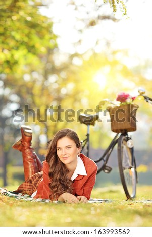 Young female lying on a grass with bicycle in a park on a sunny day