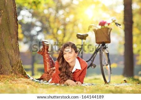 Young female lying on a green grass with bicycle in a park on a sunny day