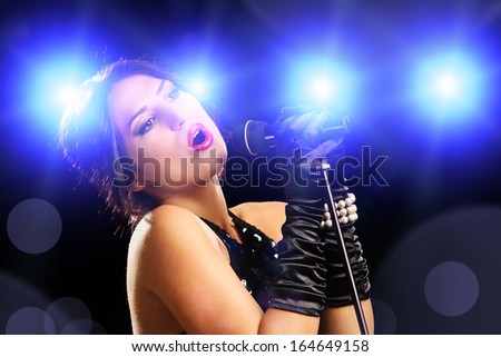 Beautiful young female singer in black dress singing on a stage