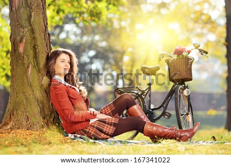 Young beautiful female with bicycle sitting on a green grass and relaxing in a park on a sunny day