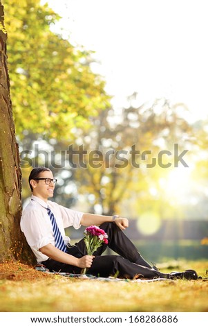 Handsome guy with a bunch of flowers sitting on a grass and relaxing on a sunny day