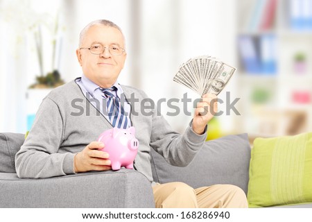 Senior gentleman sitting on a sofa and holding a piggy bank and money at home