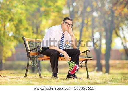 Sad guy holding a bouquet of flowers on a wooden bench in a park