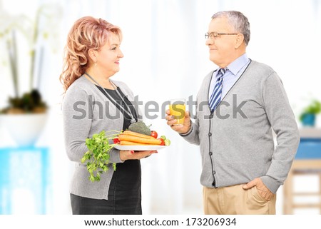Happy mature couple holding a dish full of vegetables and looking at each other, at home