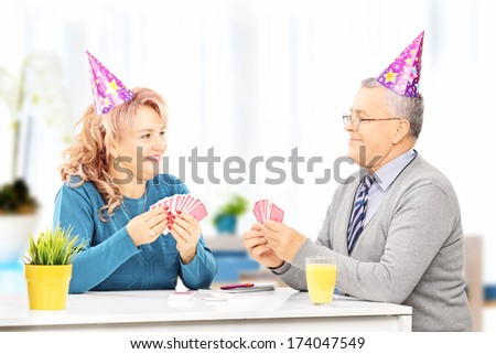 Middle aged couple with party hats sitting on table and playing cards at home