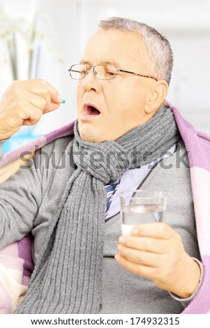 Sick man covered with blanket taking a pill, at home
