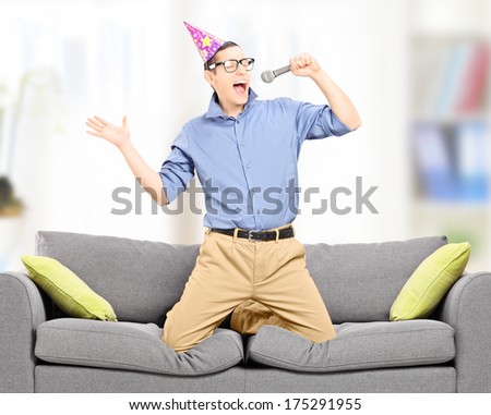 Excited young man with party hat singing on a microphone indoors, shot with tilt and shift lens