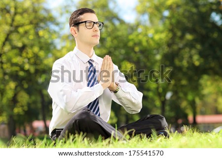 Young businessman doing yoga exercise seated on a grass in a park