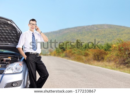 Young businessman talking on phone next to a car on an open road, shot with tilt and shift lens